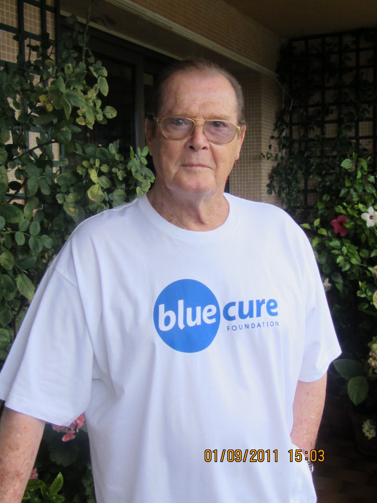 Sir Roger Moore wearing Blue Cure shirt